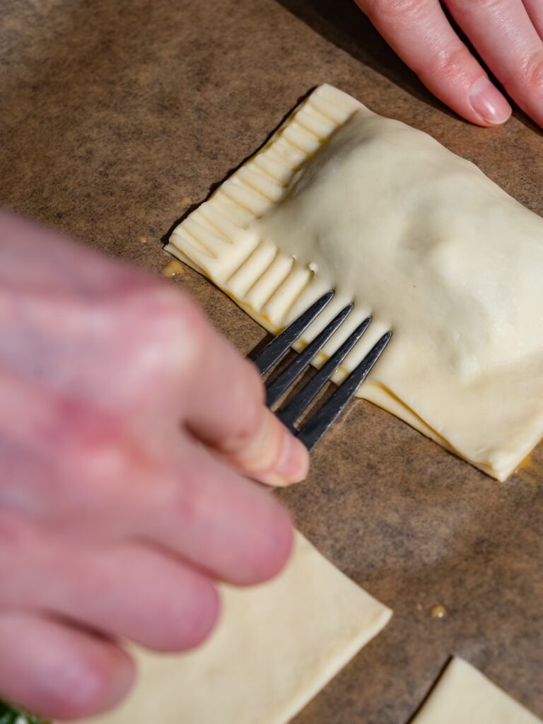 Les bords de la pâte feuilletée aux épinards et à la feta sont pressés à l'aide d'une fourchette.