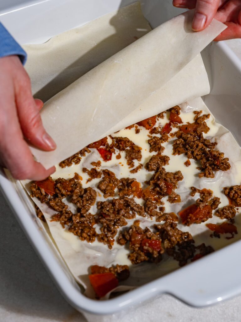 A sheet of yufka dough is placed over the sauces for the minced meat börek.