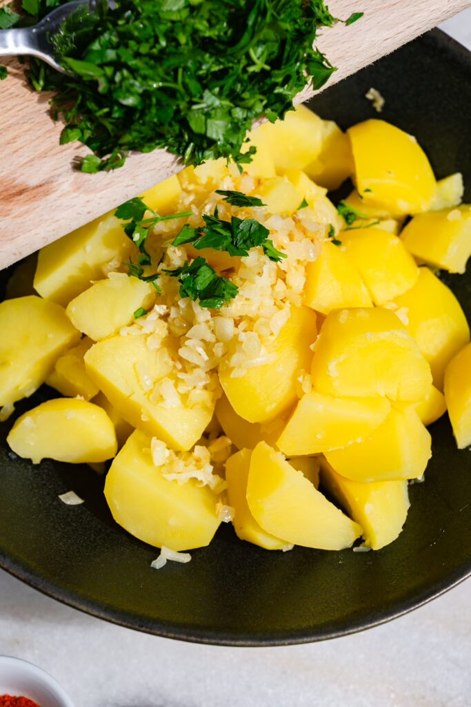 Le persil haché est ajouté aux pommes de terre, aux oignons et à l'ail.
