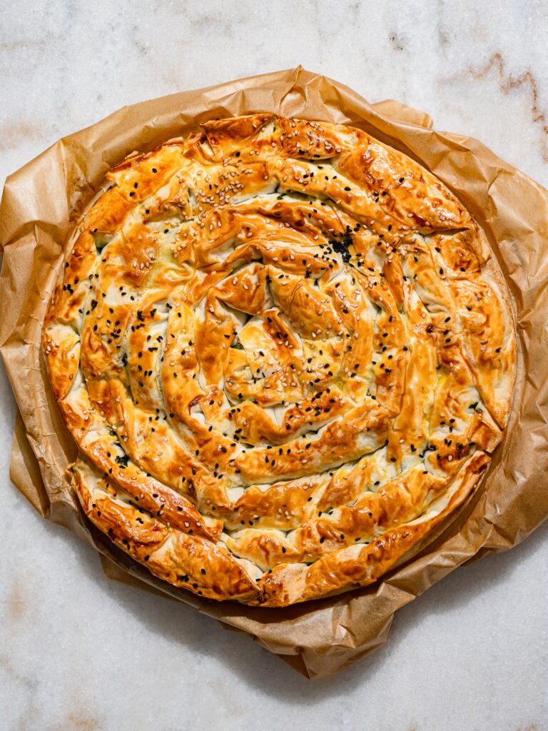 Un caracol Börek listo para hornear yace sobre papel de horno en una mesa.