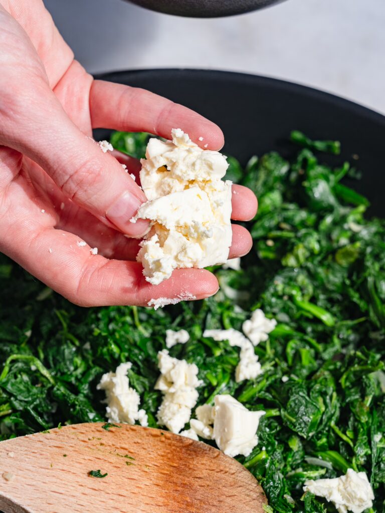 Desmenuza el queso feta en el relleno de espinacas para el börek.