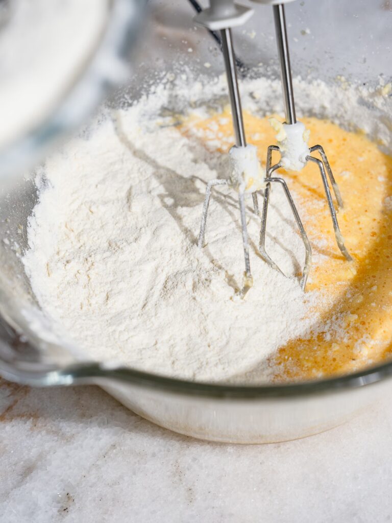 Añade la mezcla de harina a la mezcla de huevo espumosa para el pastel marmolado húmedo de la abuela en el bol.