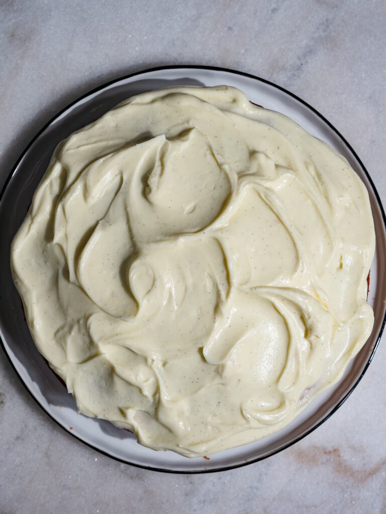 Karottenkuchen saftig und locker ist mit einem Frischkäse Frosting bestrichen und liegt in Gänze auf einem Servierteller.