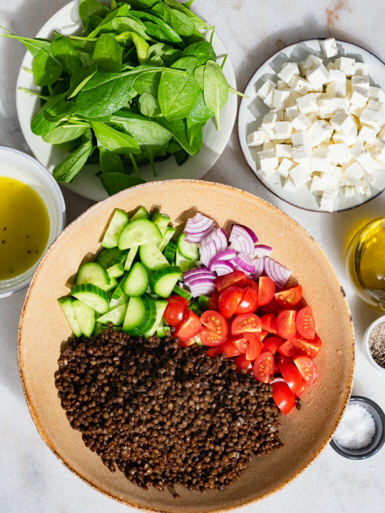 Tous les ingrédients de la salade de lentilles coupés et placés dans des petits bols sur une table.