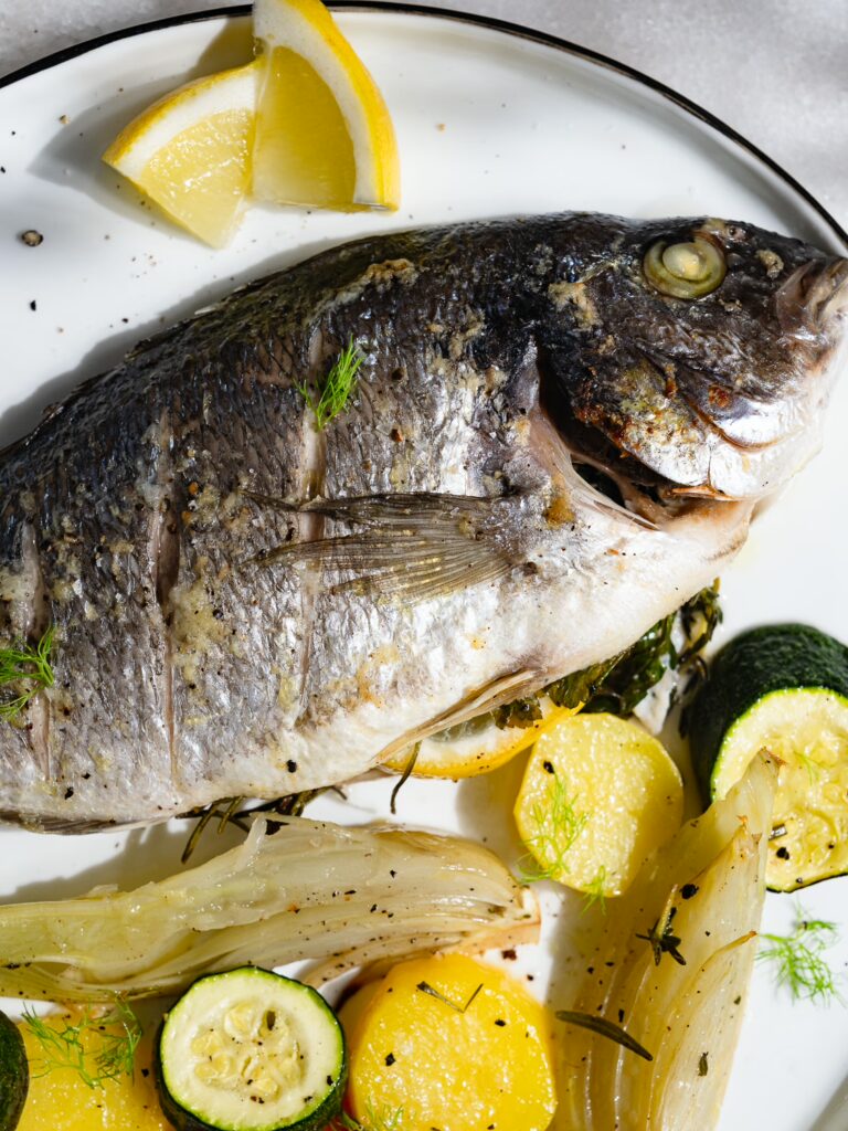 Daurade cuite au four avec des légumes au four servis sur une assiette.