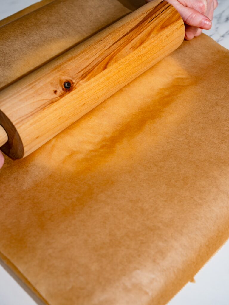 Extiende la masa entre dos hojas de papel de horno con ayuda de un rodillo.