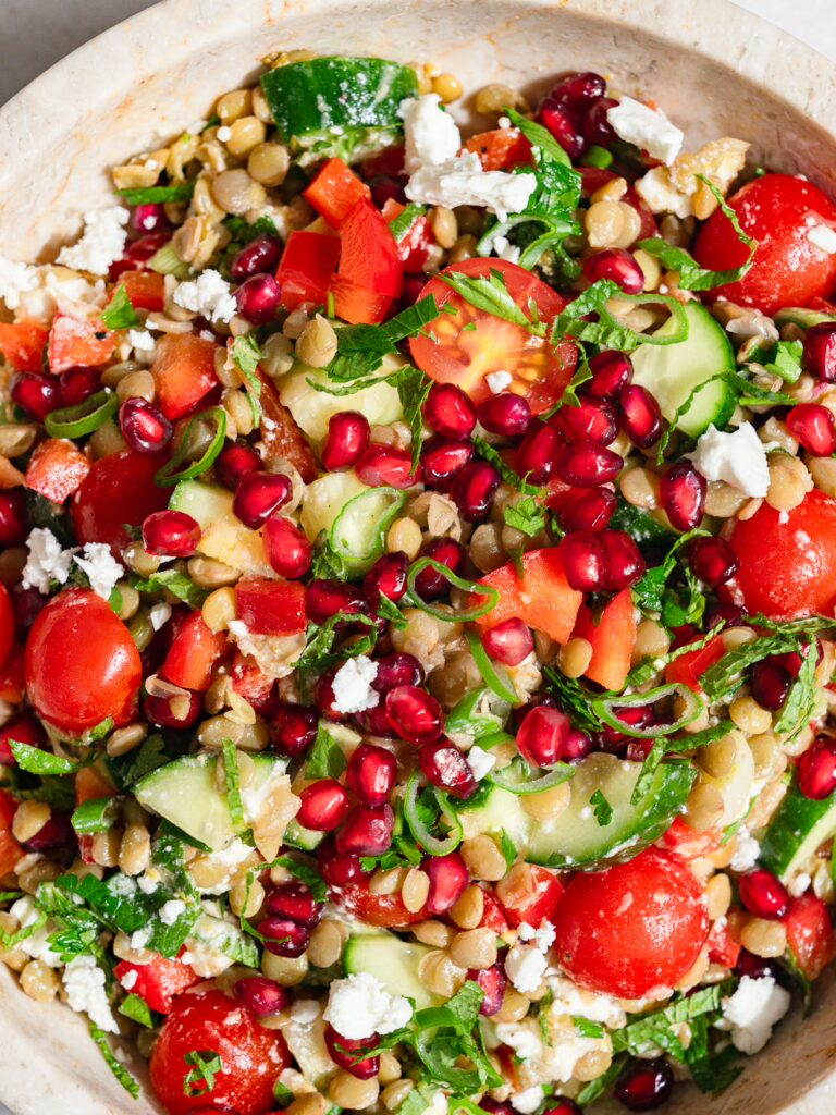 Salade de lentilles à l'orientale servie dans un bol avec de la feta et des graines de grenade.