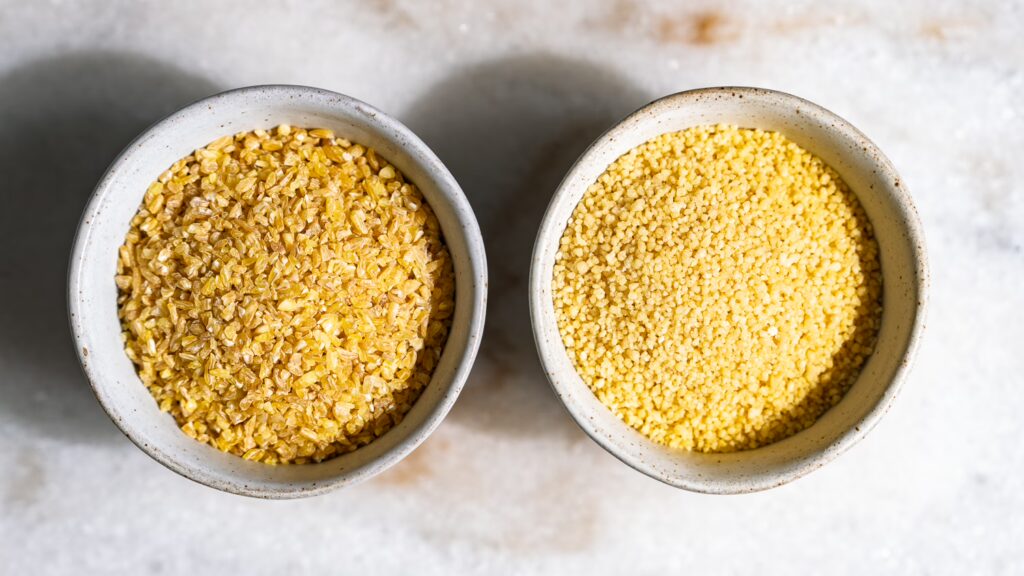 Bulgur und Cous Cous in zwei kleinen Schälchen nebeneinander, um den Unterschied darzustellen.